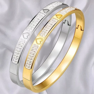Close-up of gold and silver heart-shaped bangles with crystals on silk background