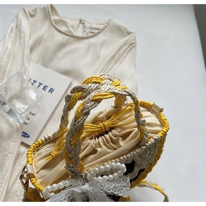 Close-up of woven straw bag showing lace bow, pearl chain and drawstring closure