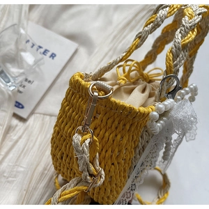 Detail of handwoven straw bucket bag with yellow contrast, pearl charms, and lace trim