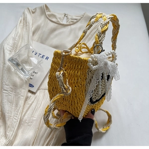 Detail of straw woven bag with yellow smile embroidery and pearl lace bow accents