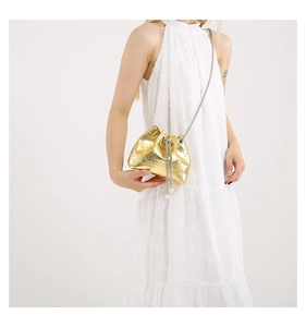 Detail of golden drawstring bucket bag with skull embossing and pearl charm accents