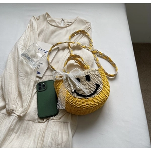 Detail of yellow woven straw beach bag featuring a black smiley face and pearl lace strap