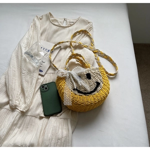 Close-up of woven straw bag with embroidered smile, lace bow and pearl charm detail