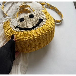 Close-up of straw woven bag with black smiley face design, lace bow and pearl charm