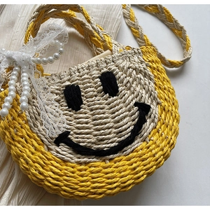 Close-up of straw woven bag with smiley face pattern, pearl beads, and lace bow details