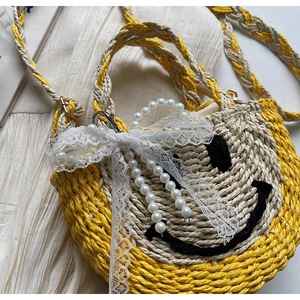 Close-up of handmade straw bag with woven smiley face, lace bow, and pearl handle details