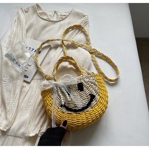 Detail of hand-woven straw bag with smiley face pattern and artificial pearl handle