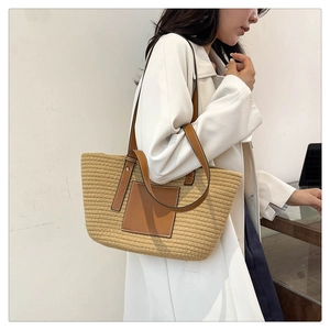 Detail of straw woven tote bag featuring brown leather straps and square patch on model