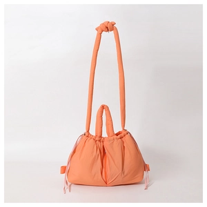 Close-up of orange quilted down-filled puffer bag with drawstring and knot strap