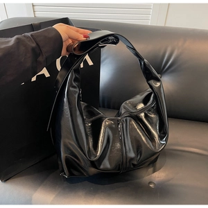 Détail d'un grand sac hobo en cuir verni noir avec bandoulière réglable et fini brillant