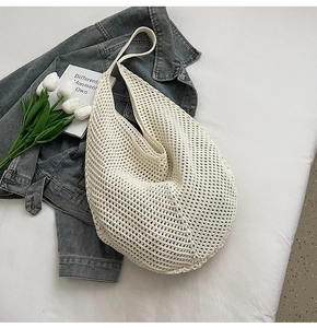 Detail view of cream crochet knit beach bag with hollow mesh design on a soft white bed
