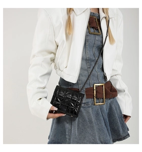Detail of a black quilted mini chain bag worn with a white jacket and blue denim skirt