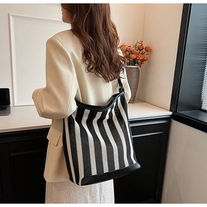 Detail of a large black and white striped tote bag featuring mesh knit and leather trim