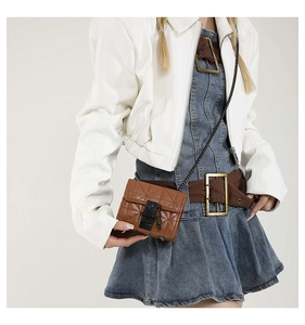 Detail of a brown quilted mini crossbody bag with glossy leather and black chain strap
