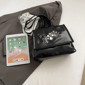 Zaino punk in pelle nera con toppe a croce, esposto con iPad e libri