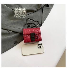 Detail of red quilted mini crossbody bag with black metal clasp on a grey blazer