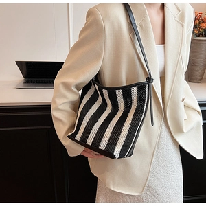 Detail view of black and white striped woven shoulder bag with leather trim on model