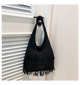 Close-up of black fringe shoulder bag with long layered tassels hanging on a door