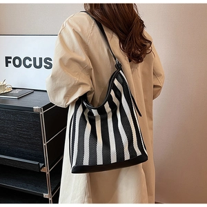 Close-up of black and white striped knit tote bag with leather trim and strap on model