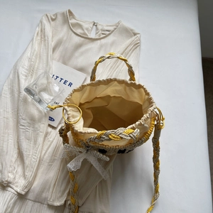 Yellow and beige straw bucket bag with lace bow and pearl charm shown from above