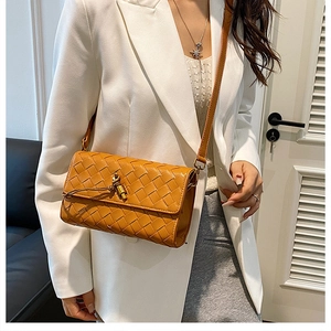 Detail of hand-woven ginger leather crossbody bag with a metal twist lock on a white suit