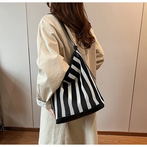 Model wearing a striped woven tote bag with black leather straps and large capacity