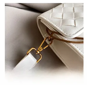 Macro detail of golden metal hook on white woven leather crossbody bag texture