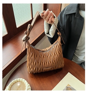Detail of a brown pleated crescent bag featuring a 3D leather bow on the shoulder strap