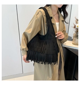 Detail view of double-layered black suede fringe shoulder bag worn with a beige trench coat