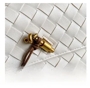Close-up of golden knot metal lock and woven leather texture on a white crossbody bag