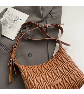 Close-up of brown pleated crossbody bag showing bow detail and leather fashion tag