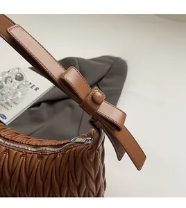 Detail of brown pleated leather shoulder bag with decorative bow and side zipper