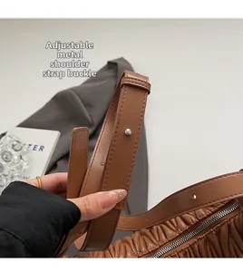 Close-up of adjustable metal buckle and zipper closure on brown pleated leather bag