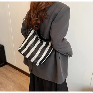Detail of striped tote bag with mesh texture and black leather strap worn by a model