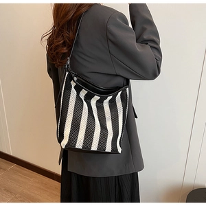 Detail of a black and white striped mesh tote bag worn over a grey blazer for work commute