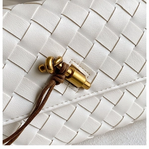 Detail of white woven leather bag featuring a gold knot clasp and brown drawstring