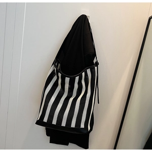 Detail of a large black and white striped tote bag showing woven texture and leather trim