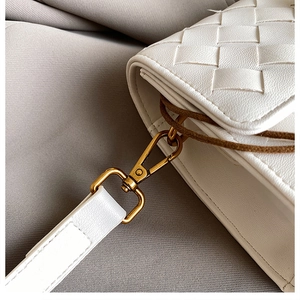 Detail of white woven crossbody bag showing leather texture and gold metal hardware hook