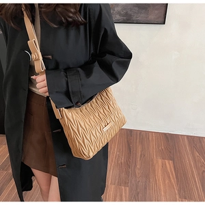 Close-up of khaki pleated crossbody bag with wavy texture on model's shoulder