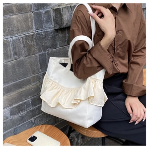 Detail of off-white canvas tote bag featuring large ruffle trim and spacious design