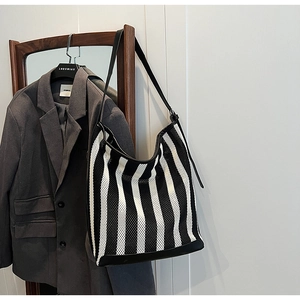 Detail of black and white striped mesh tote bag with leather trim on a wooden hanger