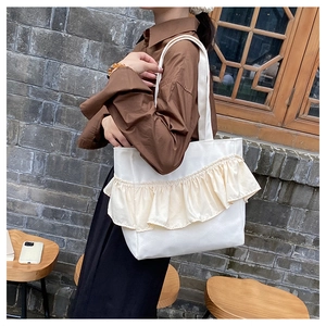 Detail view of large white canvas tote bag with beige ruffle trim and thick shoulder strap
