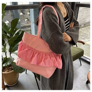 Pink canvas tote bag with ruffled pleated design shown worn over a dark cardigan