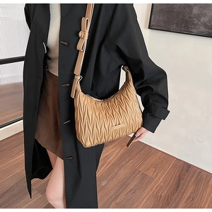 Detailed view of beige ruched leather shoulder bag with vertical stitching and metal logo
