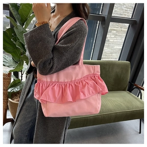 Pink canvas bucket bag with layered ruffle trim worn by a model on shoulder