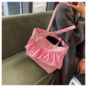 Pink canvas tote bag with ruffle details shown on a model against a green sofa