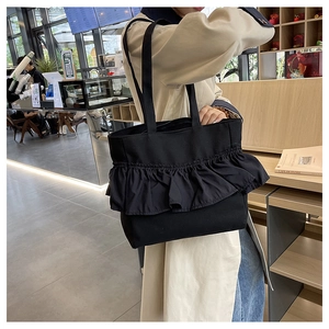 Detail of the ruffle pleated edge on a black canvas tote bag shown in a cafe setting