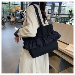 Detail of black canvas tote bag with ruffled pleats in a cafe setting with soft natural light