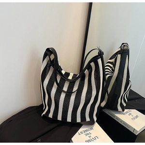 Detail of black and white striped mesh tote bag with leather straps on a mirrored surface