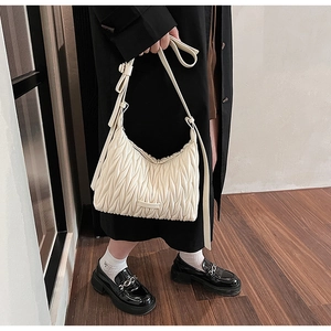 Detail of a creamy white pleated shoulder bag with adjustable strap and textured leather finish